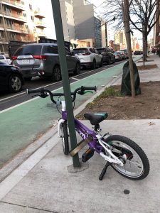 A child's woom bicycle parked with a TiGr lock in New York in front of a parking-protected bike lane