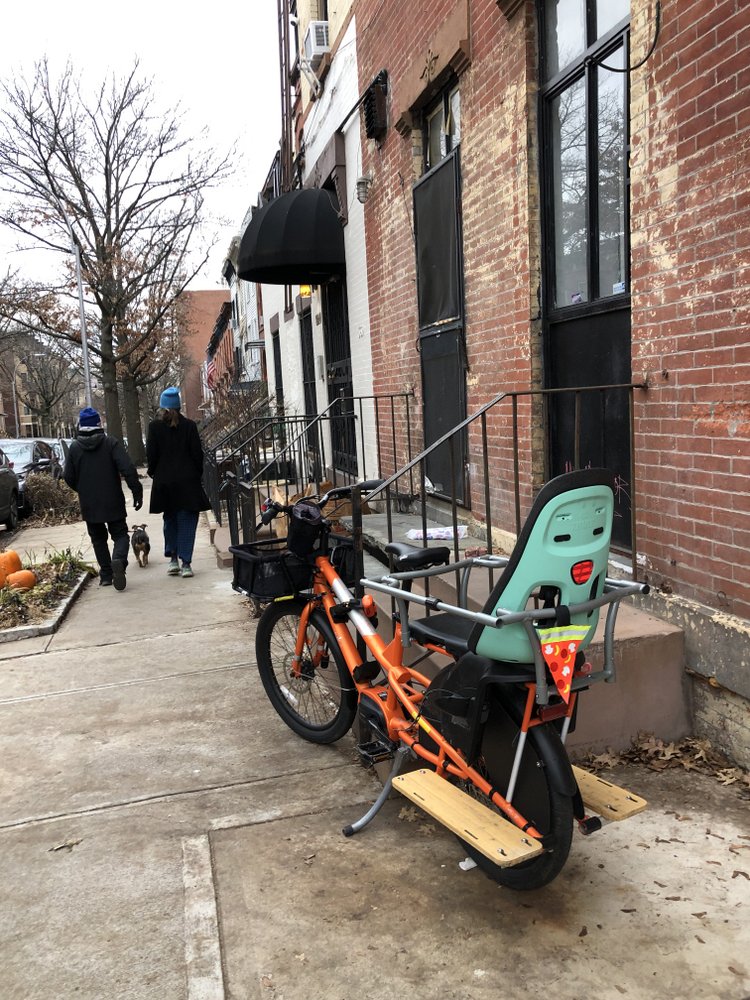 Orange Yuba Kombi e-bike with child seat and safety pizza reflector