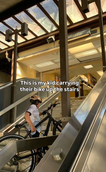 Child carrying bike up stairs at BART station, captioned "This is my kid carrying their bike up the stairs"